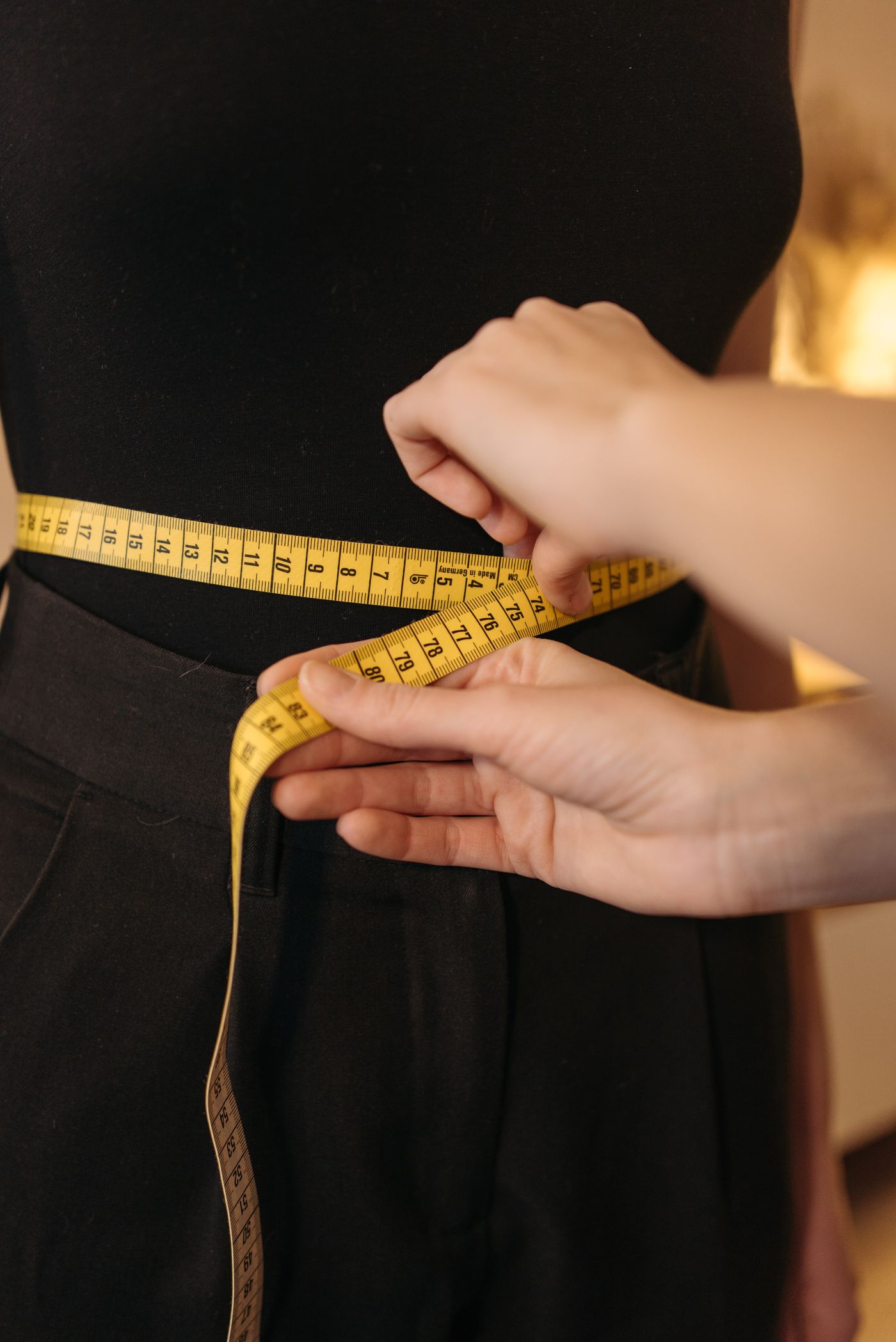 Hands checking a waist measurement with a yellow tape measure